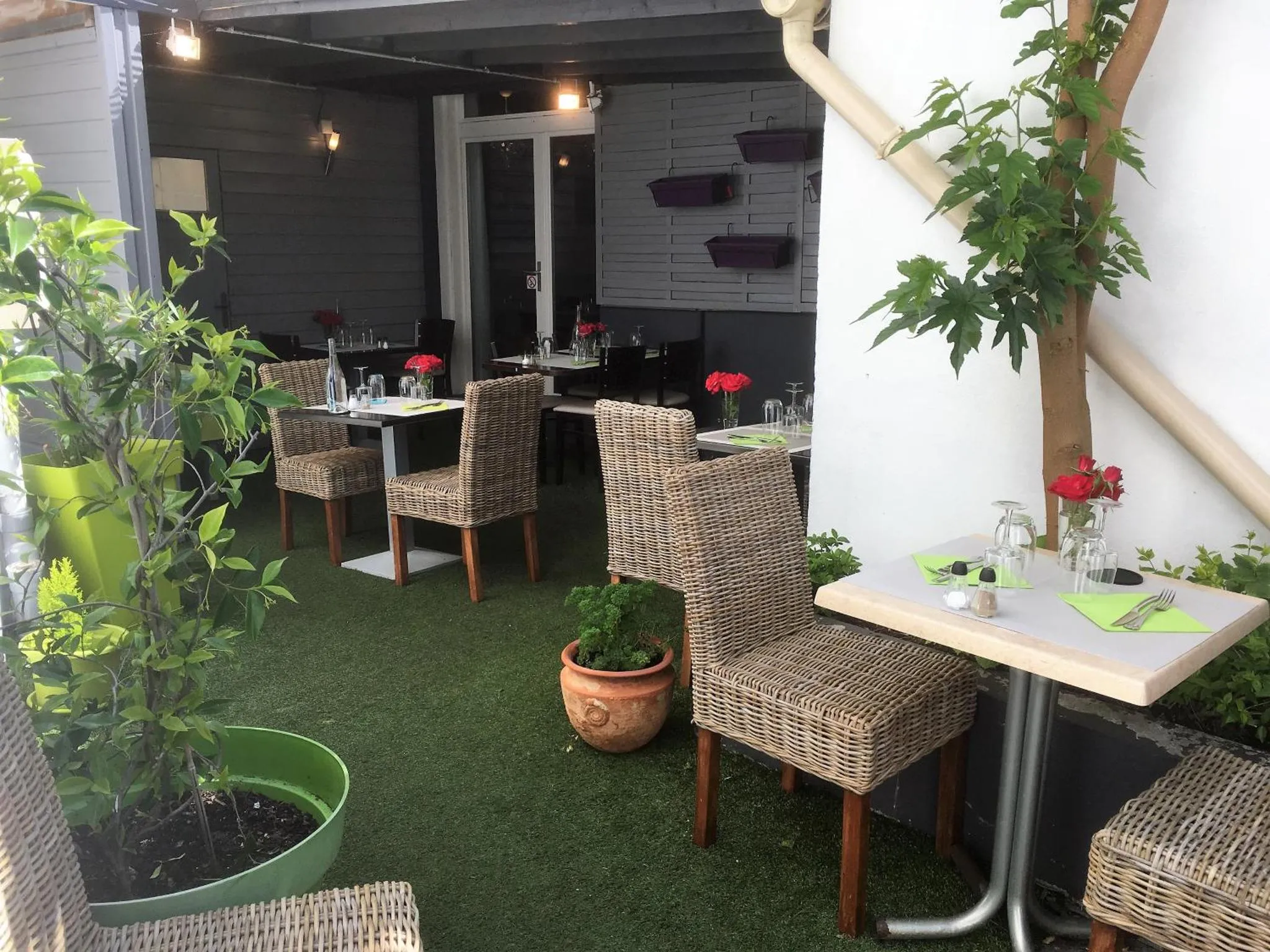Tables et chaises en osier disposées sur une terrasse verdoyante.