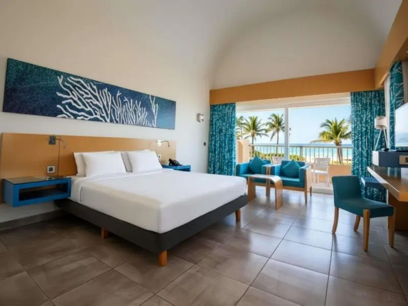 Chambre lumineuse avec un grand lit et un coin salon donnant sur la mer.