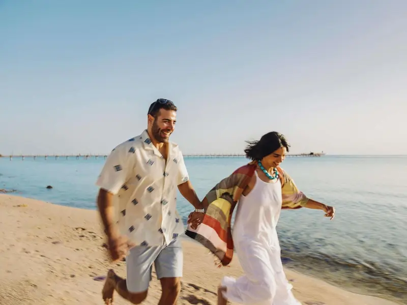Un couple souriant se promène main dans la main sur une plage de sable fin.
