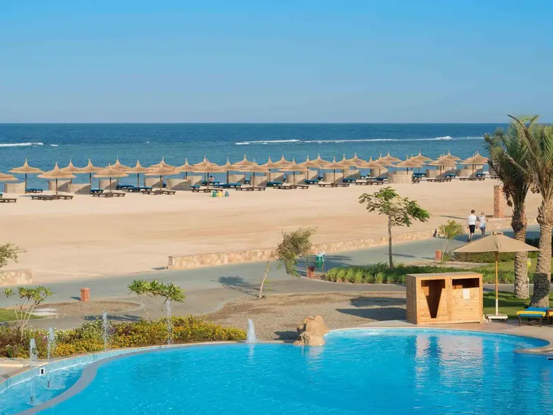 Vue aérienne d'une plage de sable fin avec parasols et d'une piscine turquoise.