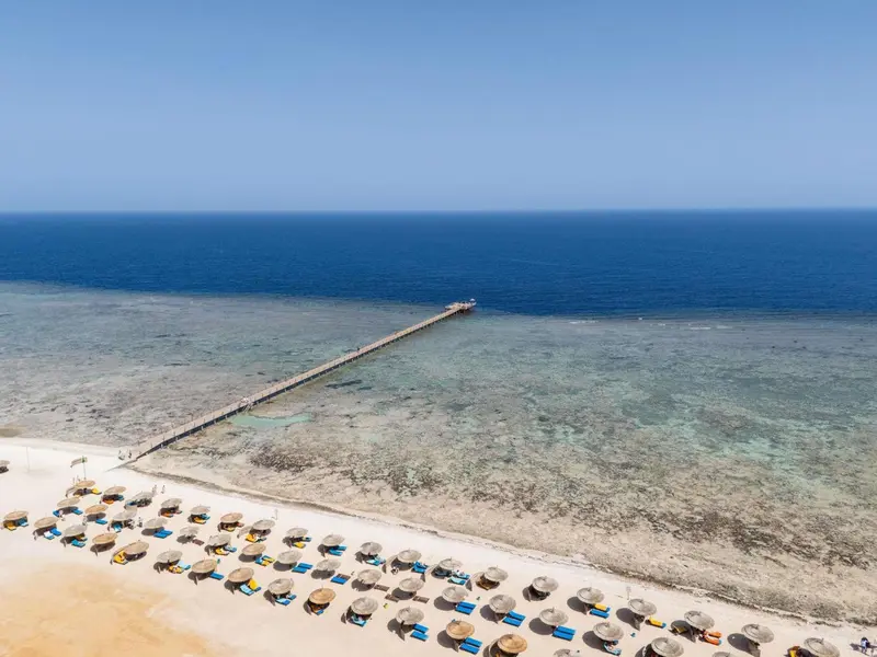 Vue aérienne d'une plage de sable clair bordée d'une eau turquoise et d'une jetée en bois.