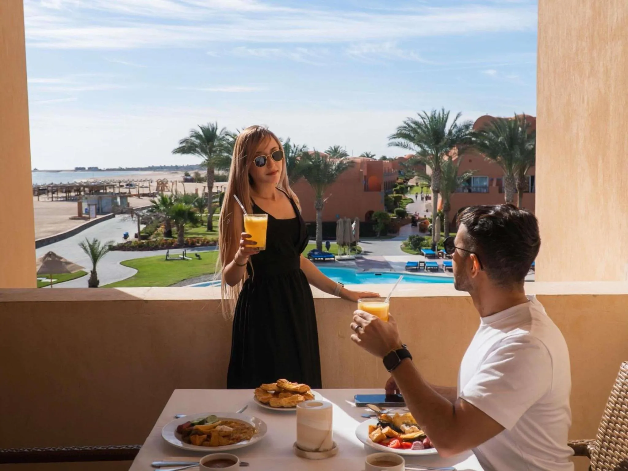 Un couple prend son petit-déjeuner sur une terrasse avec vue sur la mer et une piscine.