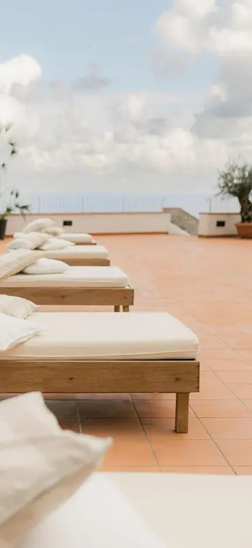 Transats blancs disposés sur une terrasse carrelée avec vue sur la mer.