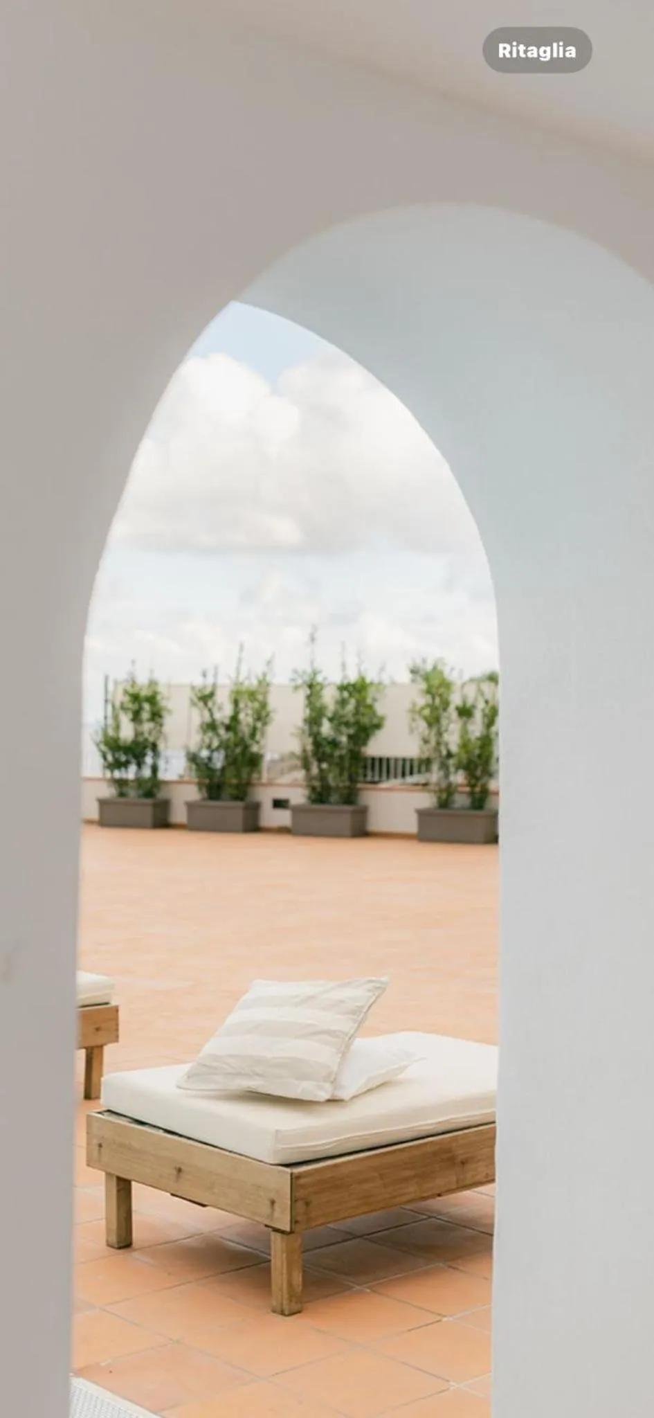 Un coussin blanc repose sur un banc en bois devant une terrasse carree.