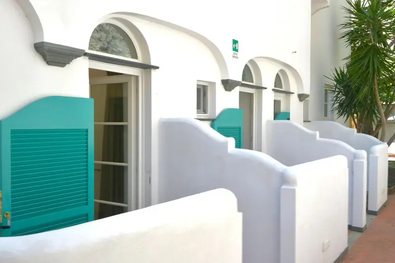 Façade blanche d'un bâtiment avec des ouvertures turquoise et des plantes vertes.