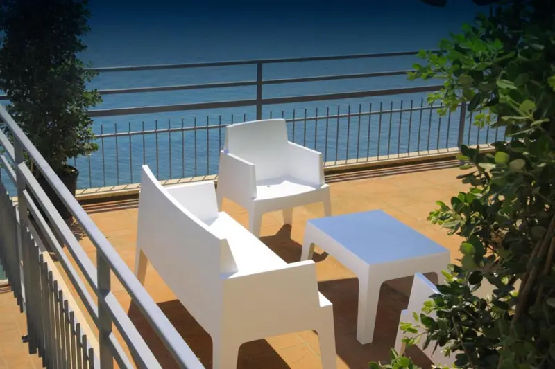 Mobilier blanc sur une terrasse ensoleillée avec vue sur la mer.