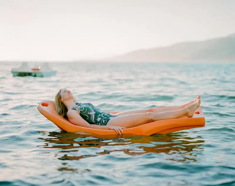 Une femme se détend sur un flotteur orange dans une mer calme.