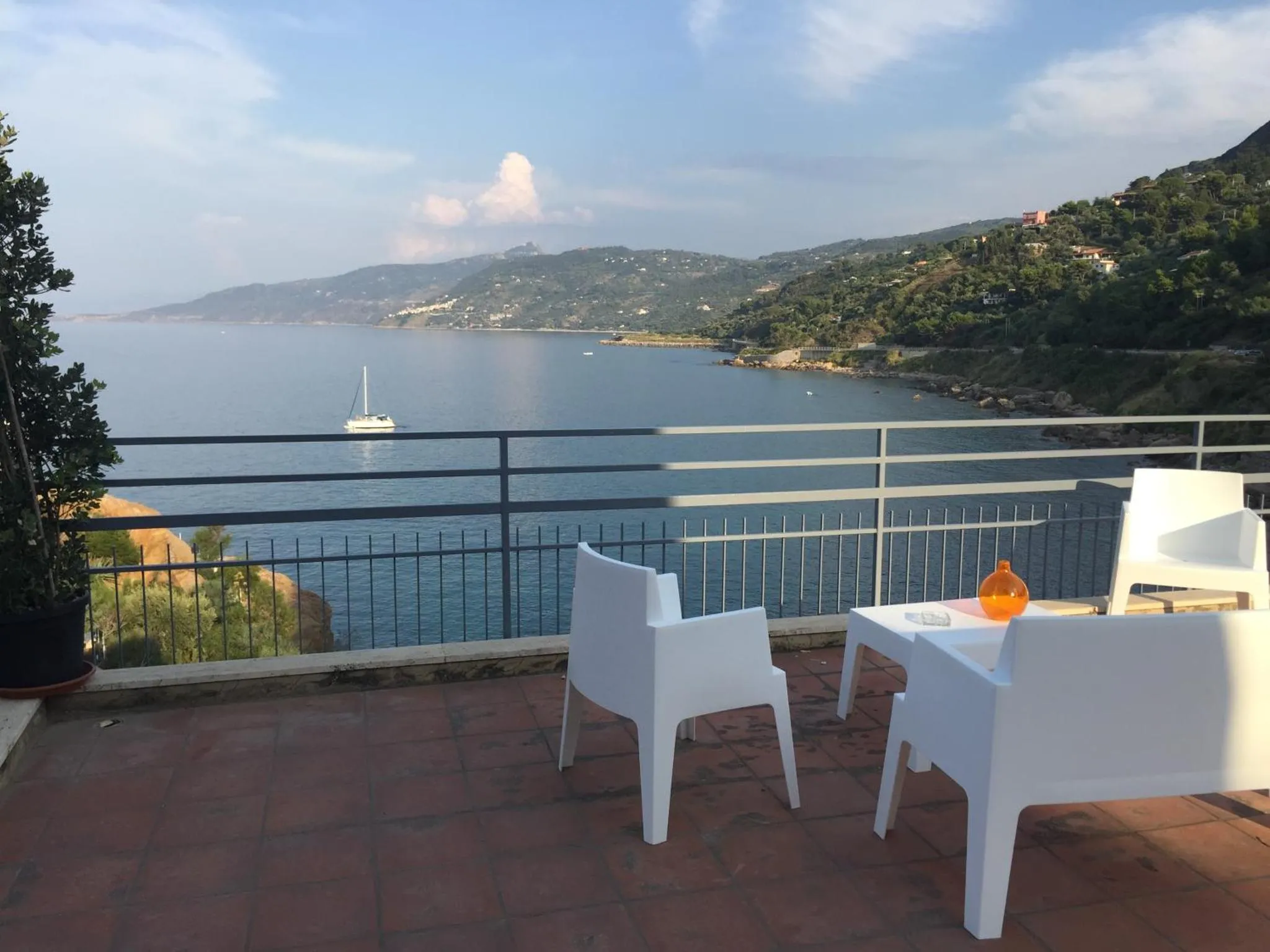 Terrasse avec mobilier blanc donnant sur une vue mer et des collines verdoyantes.