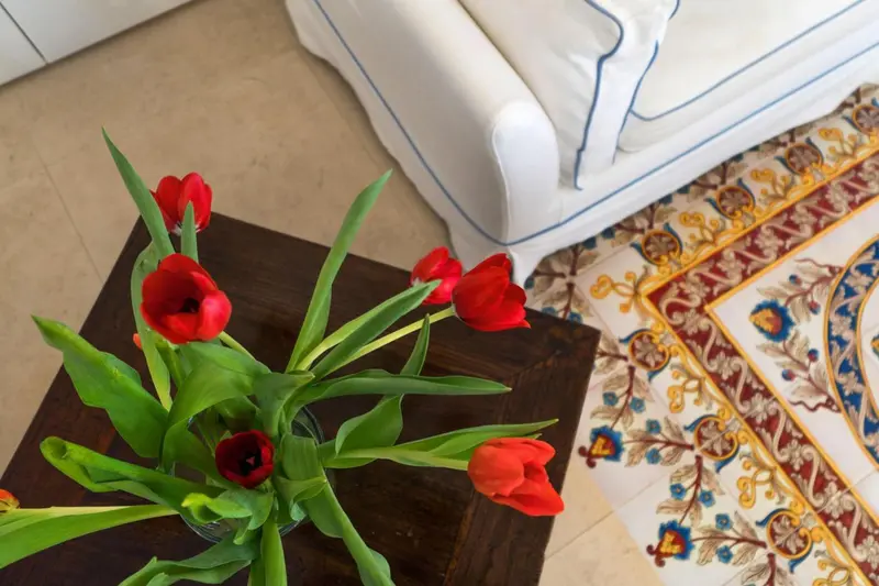 Un bouquet de tulipes rouges dans un vase sur une table basse devant un canapé et un tapis.