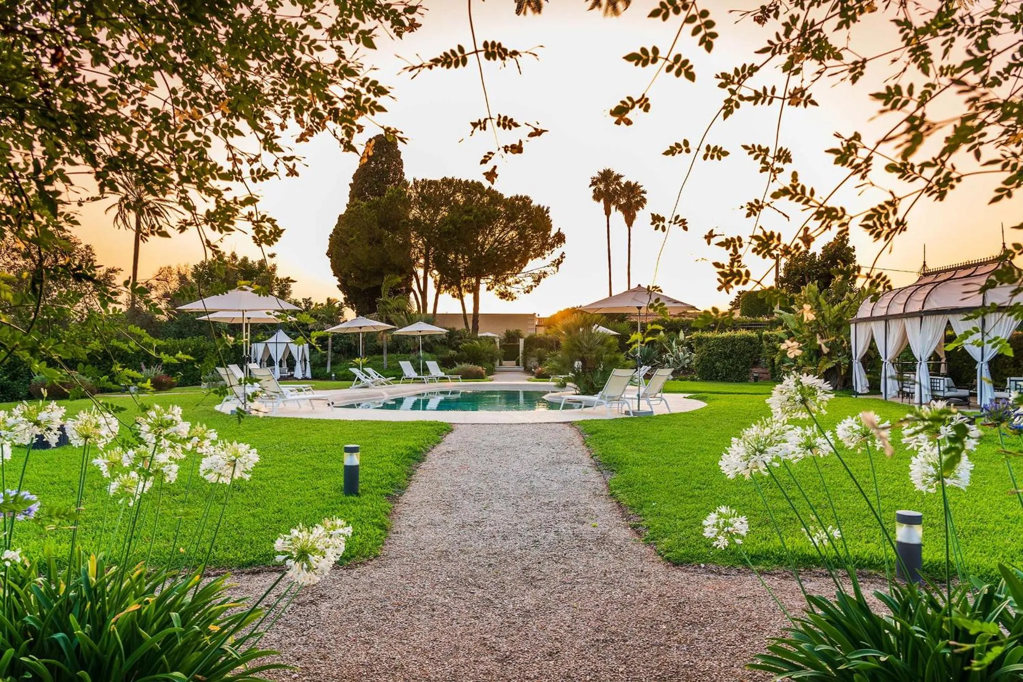 Un jardin verdoyant mène à une piscine entourée de transats et de parasols.