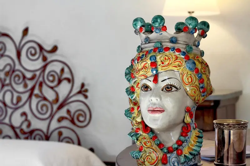 Une tête de poupée en céramique colorée repose sur un lit blanc.