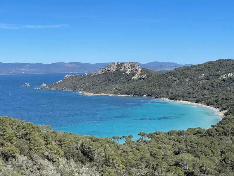 Vue aérienne d'une crique turquoise bordée de végétation et de rochers.