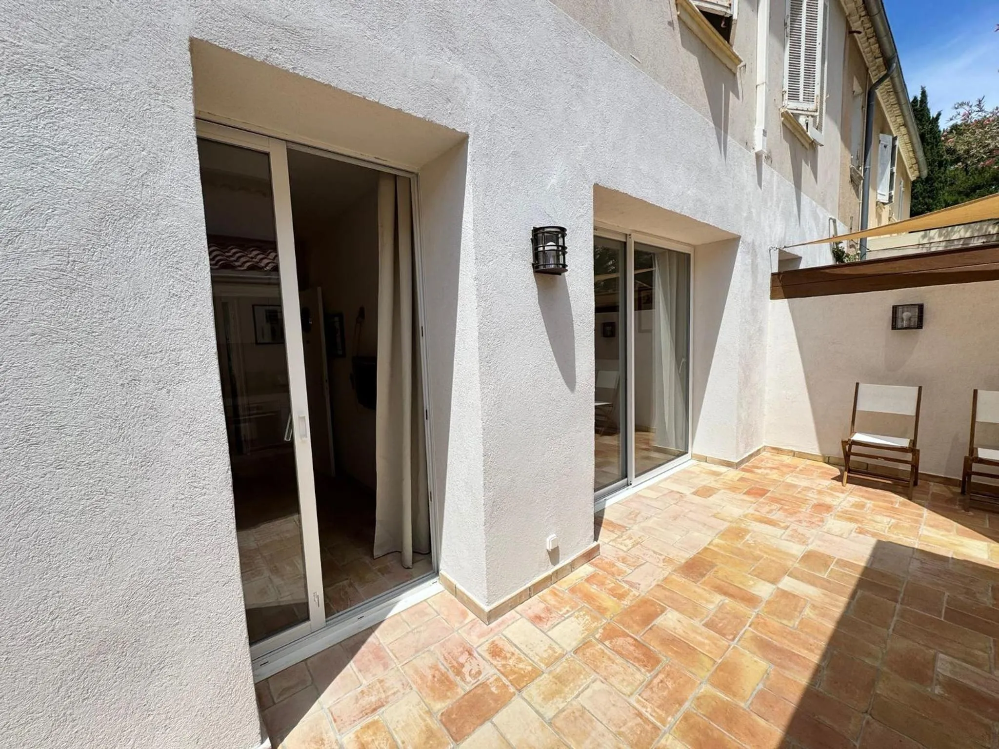 Terrasse carrelée avec des baies vitrées ouvertes sur une pièce intérieure.