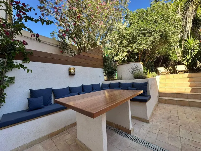 Une table en bois est entourée de sièges capitonnés bleus dans un espace extérieur pavé.
