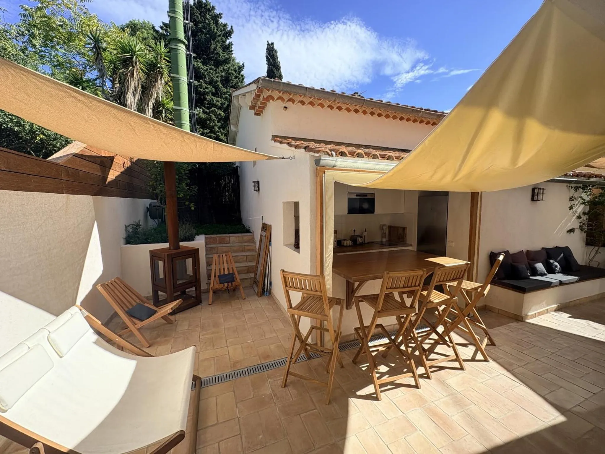 Terrasse ombragée avec mobilier de jardin et un bar en bois.