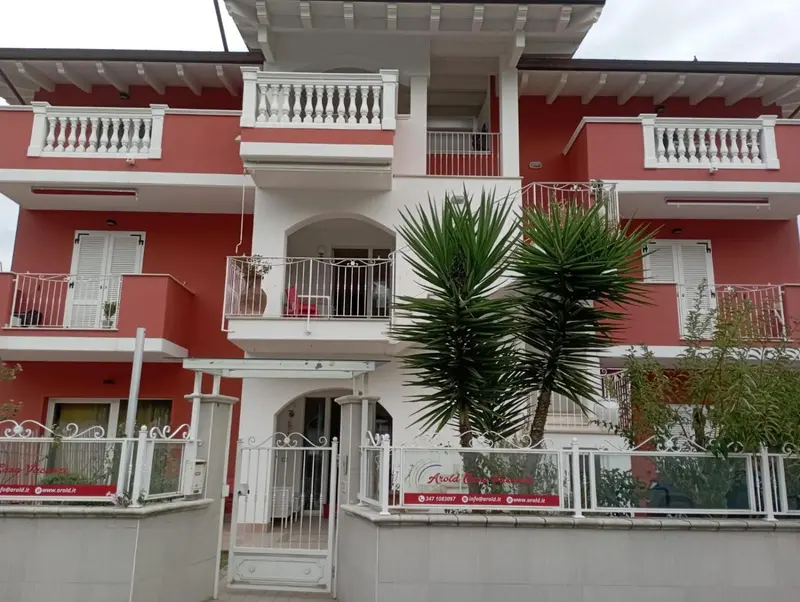 Façade d'un bâtiment rouge à deux étages avec des balcons et une végétation tropicale.