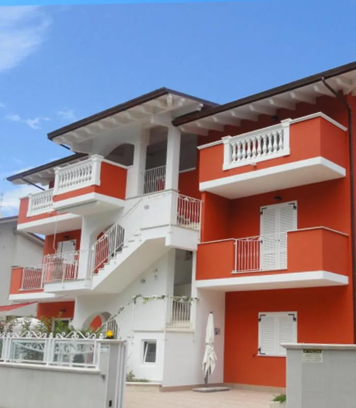 Facade d'un bâtiment rouge à balcons blancs sous un ciel bleu.