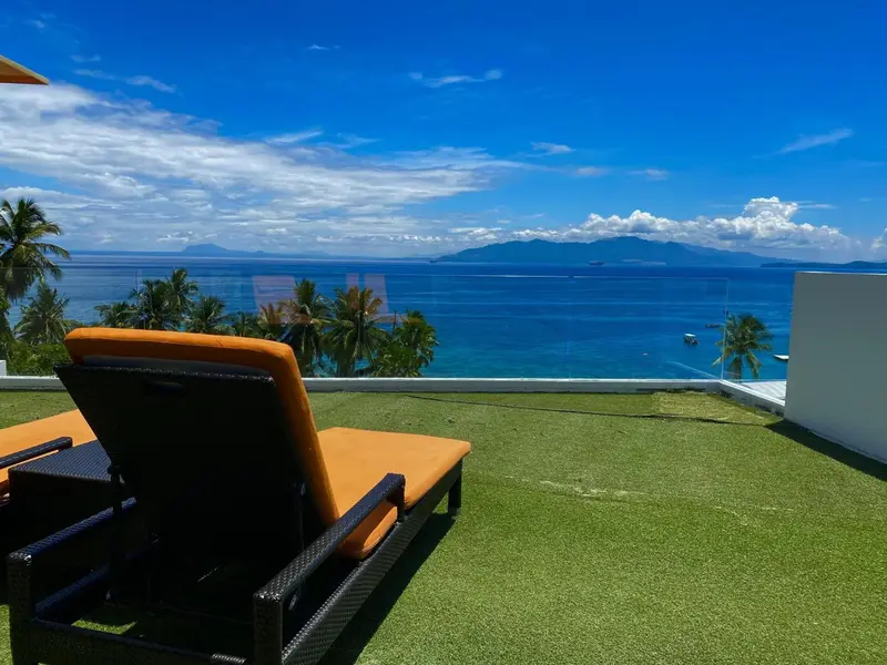 Deux transats oranges et noirs sur une terrasse verdoyante avec vue sur la mer et les montagnes.