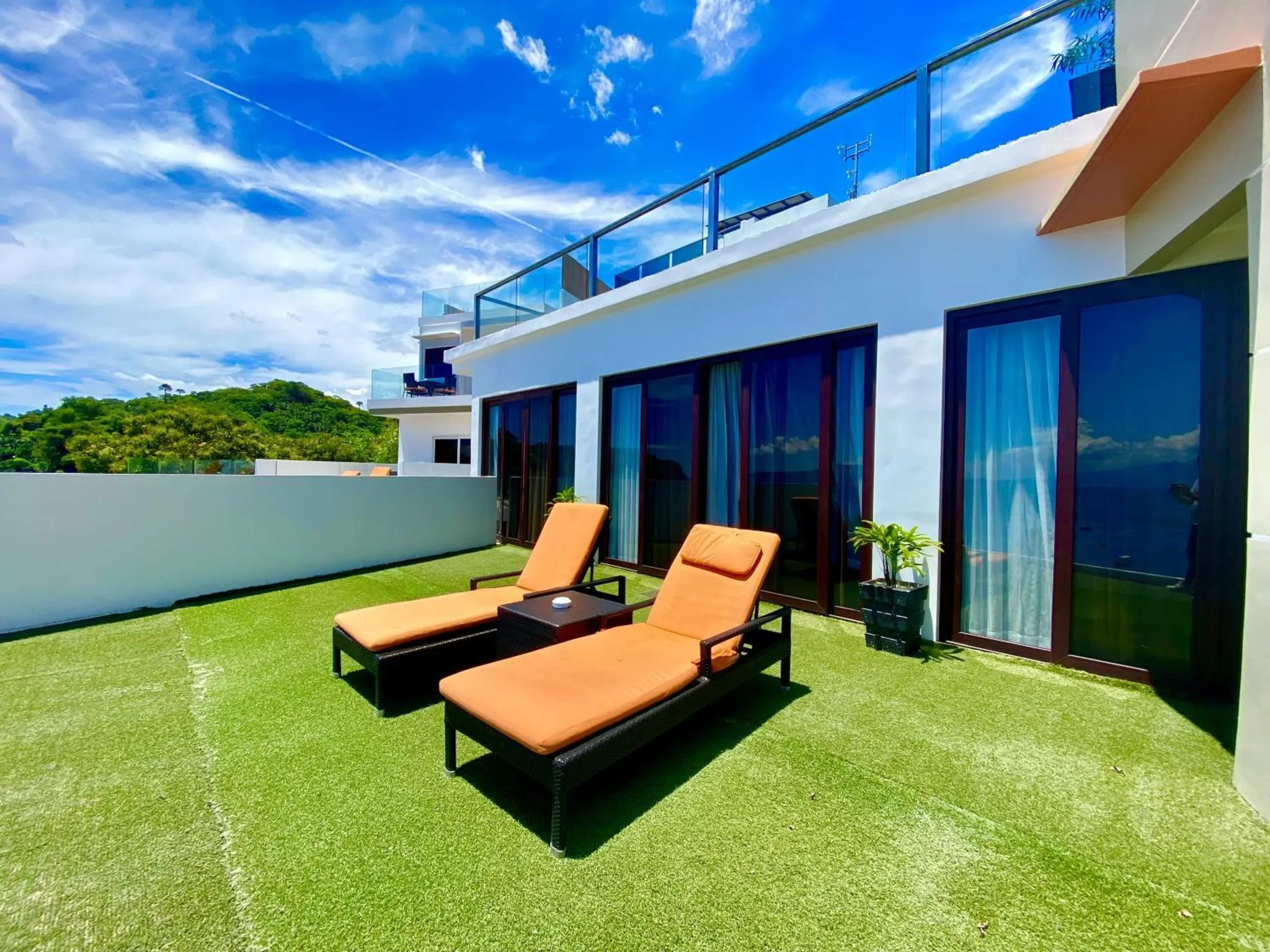 Deux transats orange sur une terrasse avec gazon synthétique et vue sur la mer.