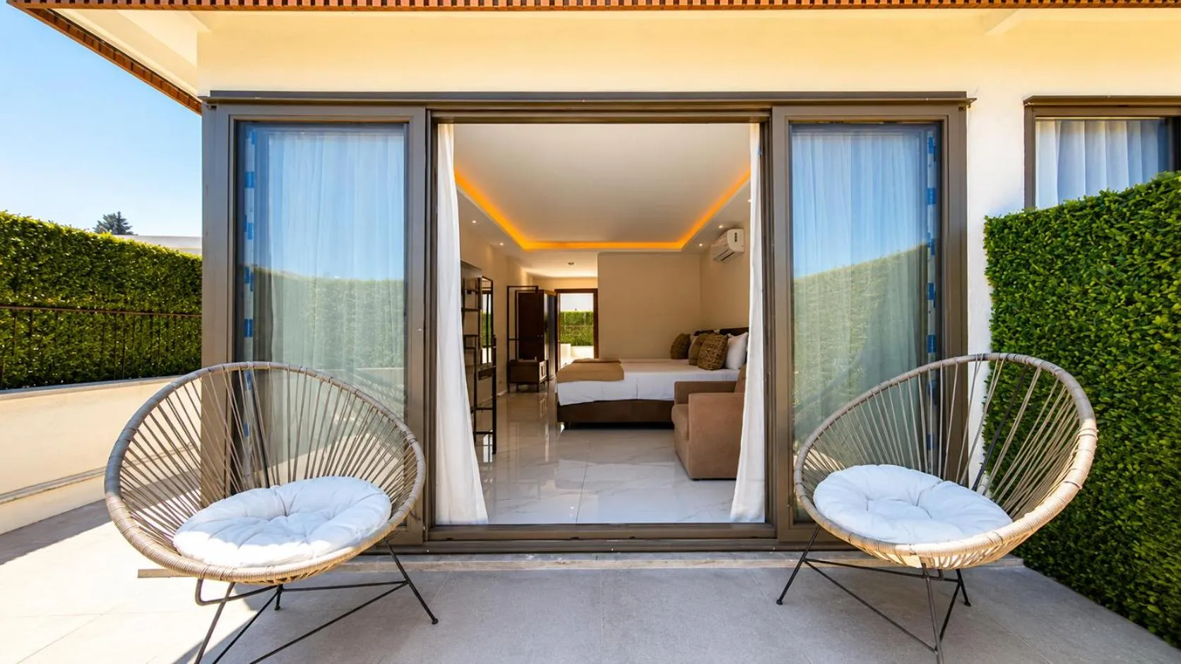 Terrasse avec deux fauteuils en osier donnant sur une chambre lumineuse.