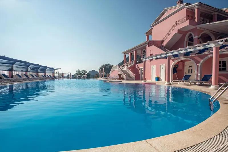 Une piscine bleue bordée de transats devant un bâtiment rose.