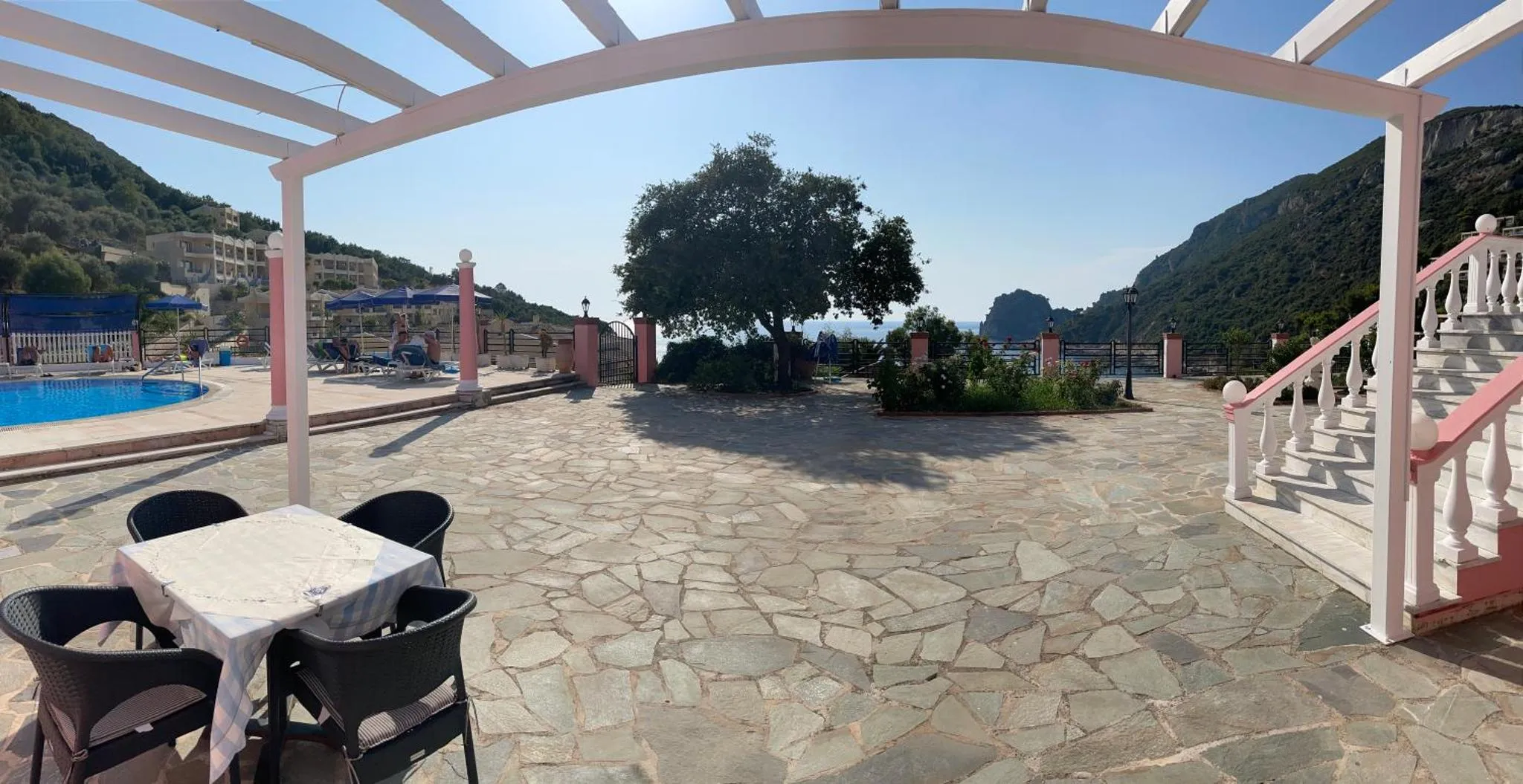 Terrasse pavée avec table et chaises devant une piscine et une vue sur la mer.