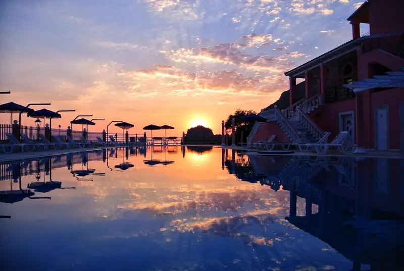 Une piscine reflète les couleurs d'un coucher de soleil sur un bâtiment.