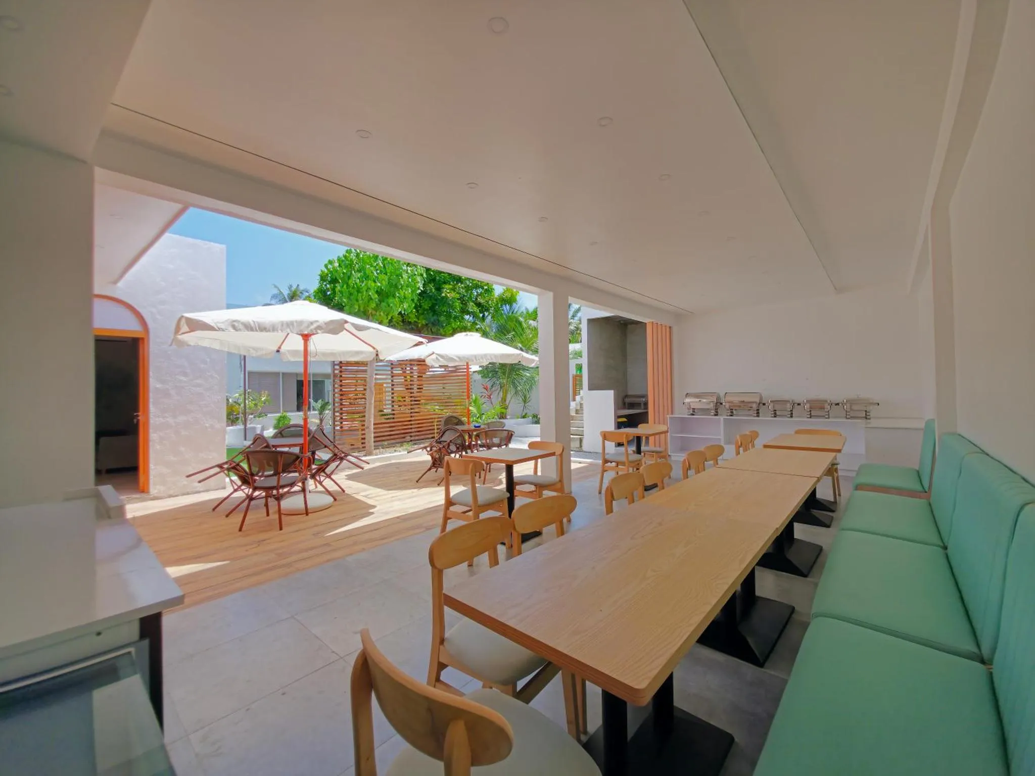 Une salle à manger lumineuse s'ouvre sur une terrasse ombragée avec des tables et des parasols.