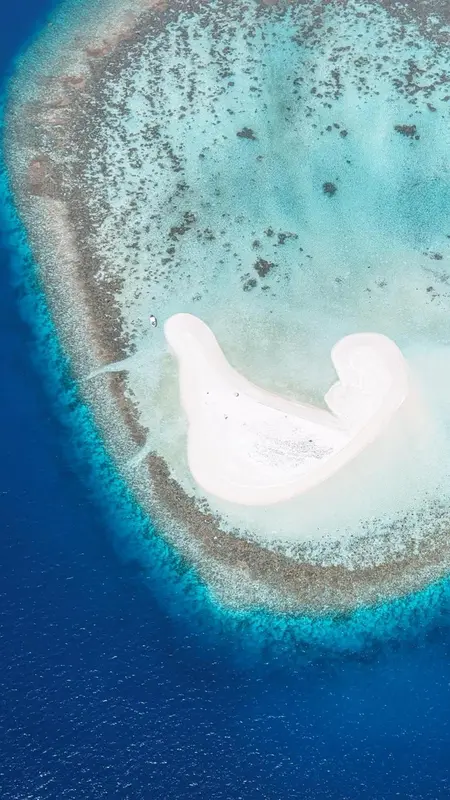 Vue aérienne d'un îlot de sable blanc entouré d'un récif corallien turquoise.