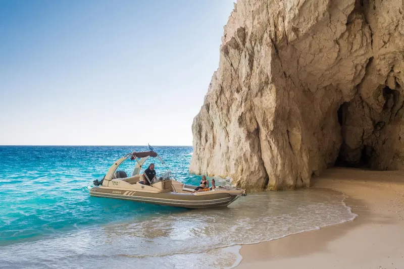 Un bateau de plaisance navigue près d'une falaise rocheuse et d'une plage de sable.