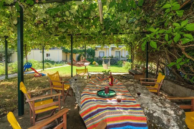 Une table colorée est dressée sous une pergola végétalisée, avec des chaises autour.