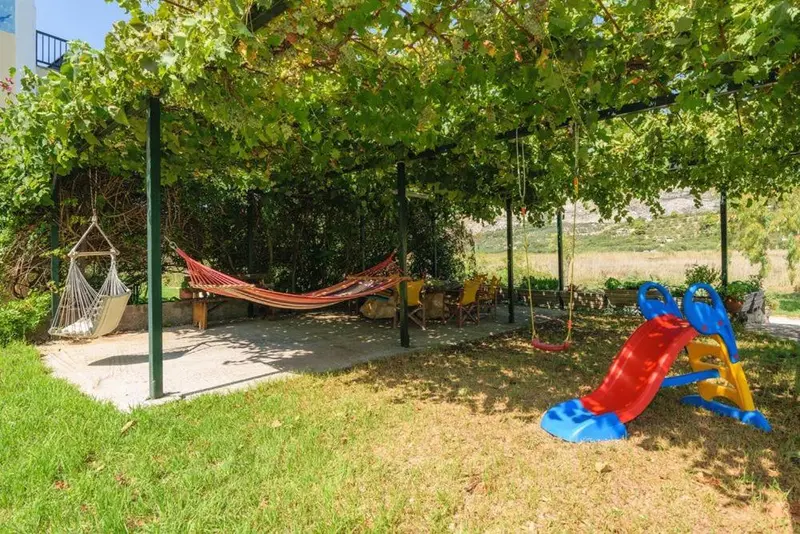 Un hamac est suspendu sous une tonnelle verdoyante, à côté d'une aire de jeux pour enfants.
