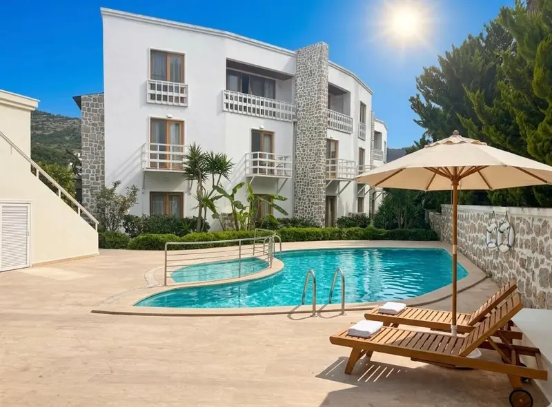 Bâtiment blanc à plusieurs étages avec piscine et transats ensoleillés.