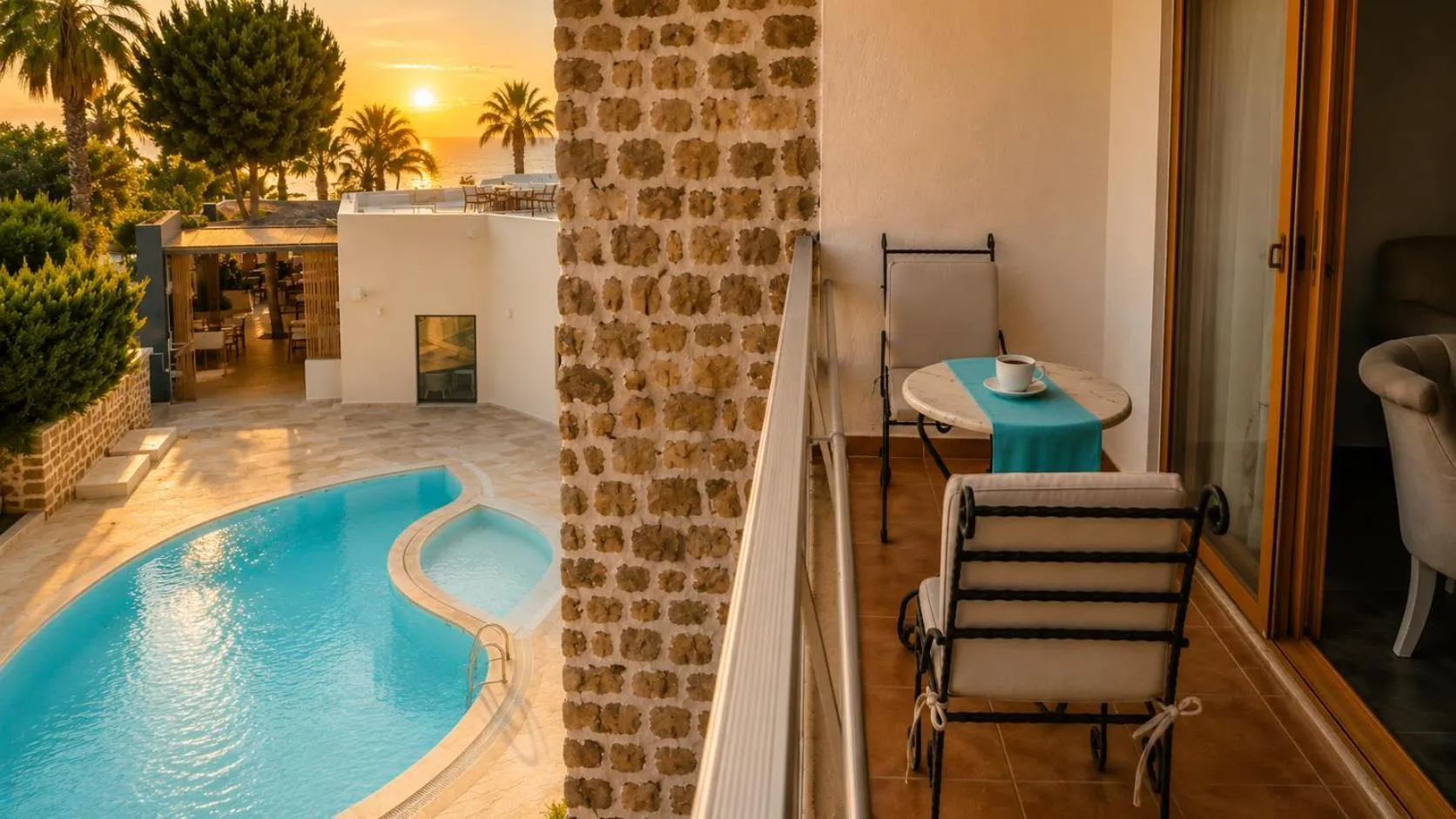 Une terrasse avec table et chaises offre une vue sur une piscine et un coucher de soleil.