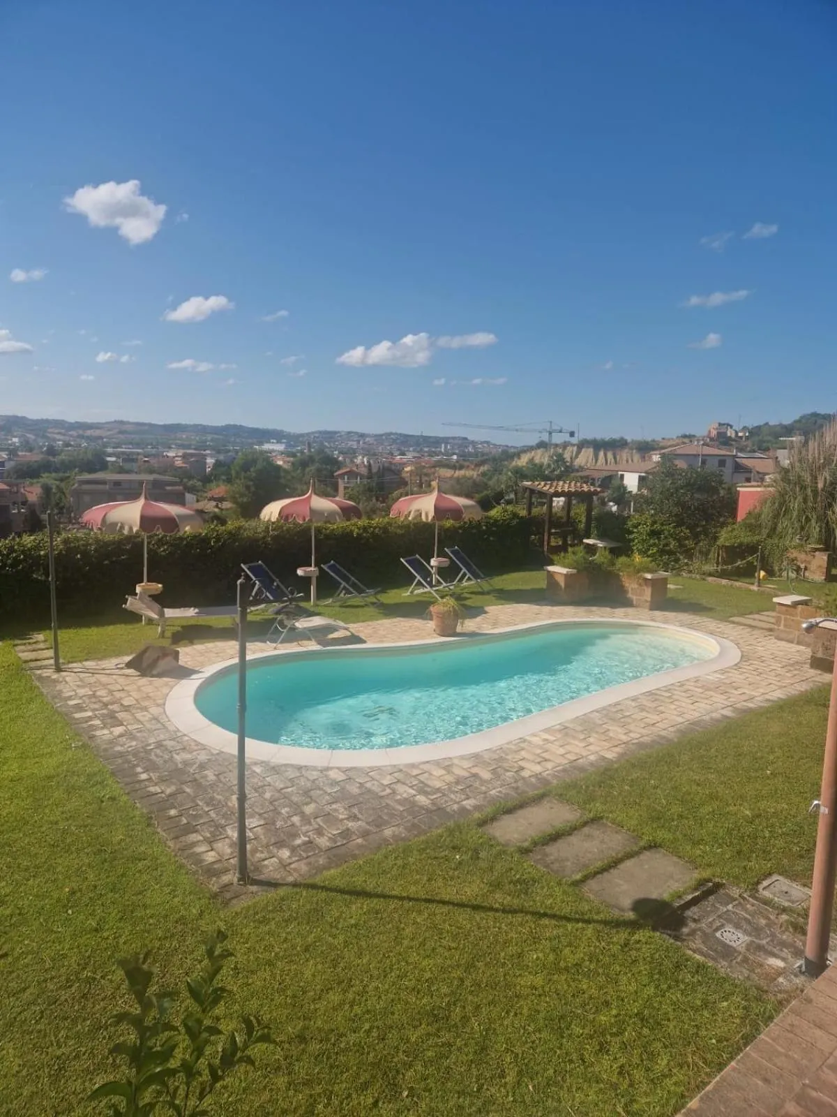 Une piscine rectangulaire entourée d'une pelouse et de transats sous des parasols.