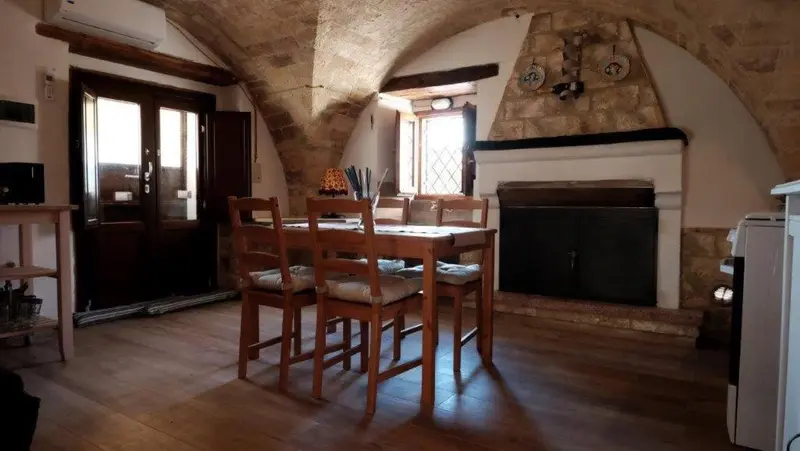 Une table en bois est entourée de chaises dans une pièce voûtée en pierre.