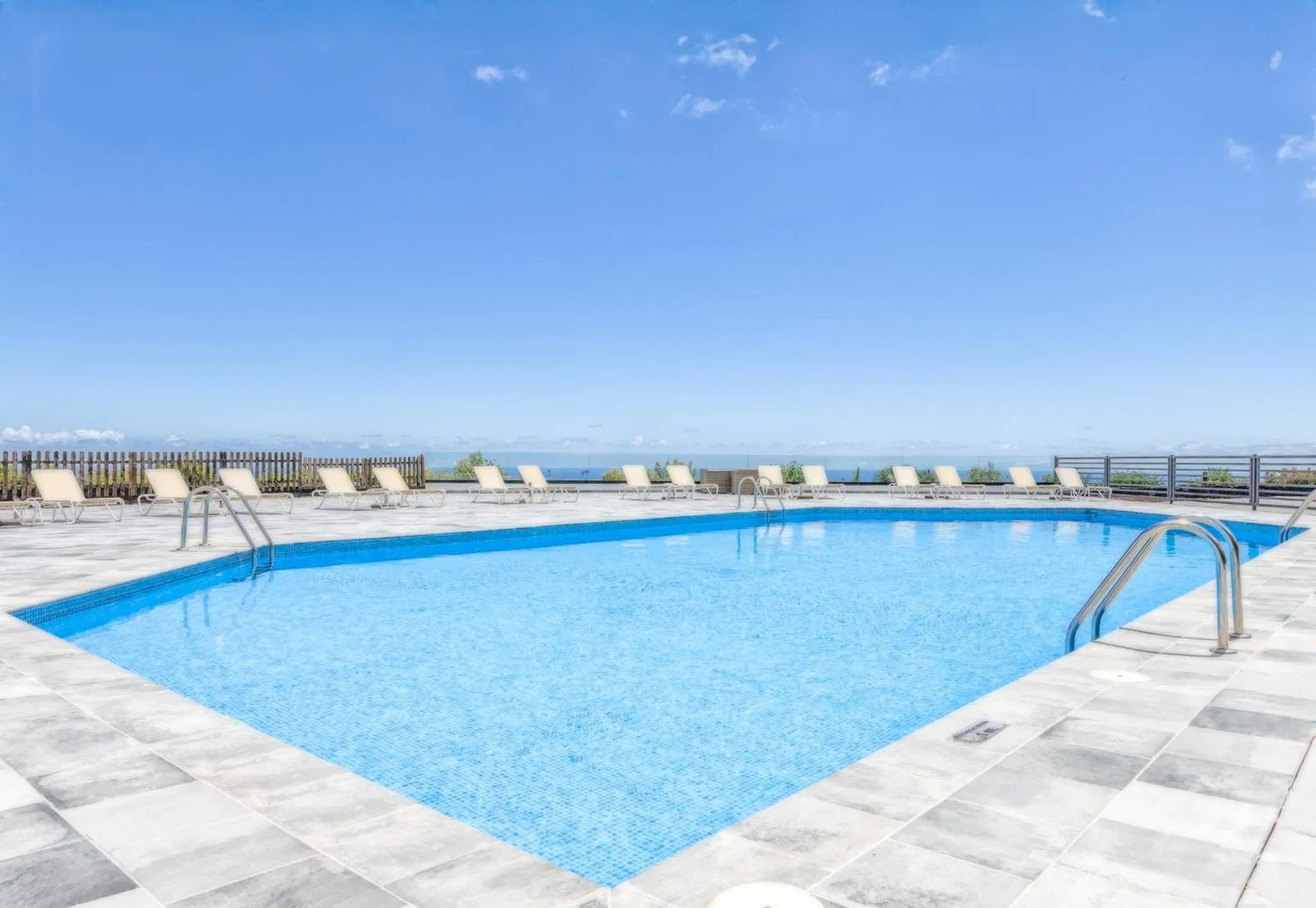 Une piscine rectangulaire bleue avec des transats sur une terrasse ensoleillée.