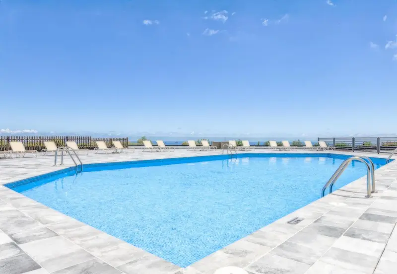 Une piscine rectangulaire bleue avec des transats sur une terrasse ensoleillée.