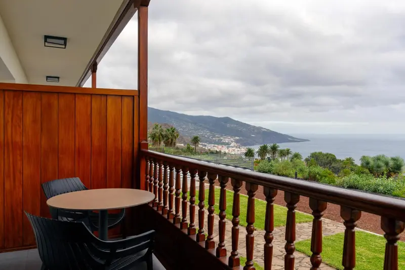Une terrasse avec table et chaises offre une vue sur un paysage montagneux et la mer.