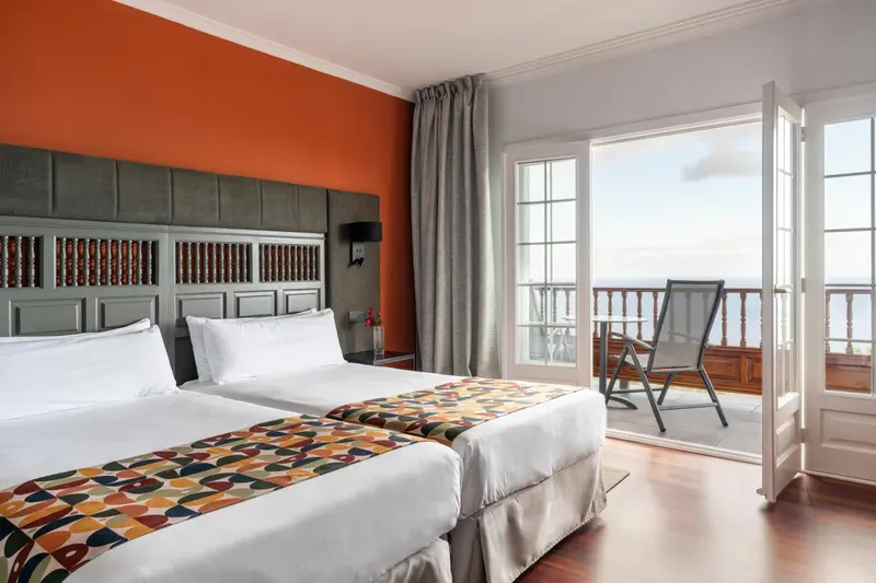 Une chambre lumineuse avec un grand lit et un balcon donnant sur la mer.