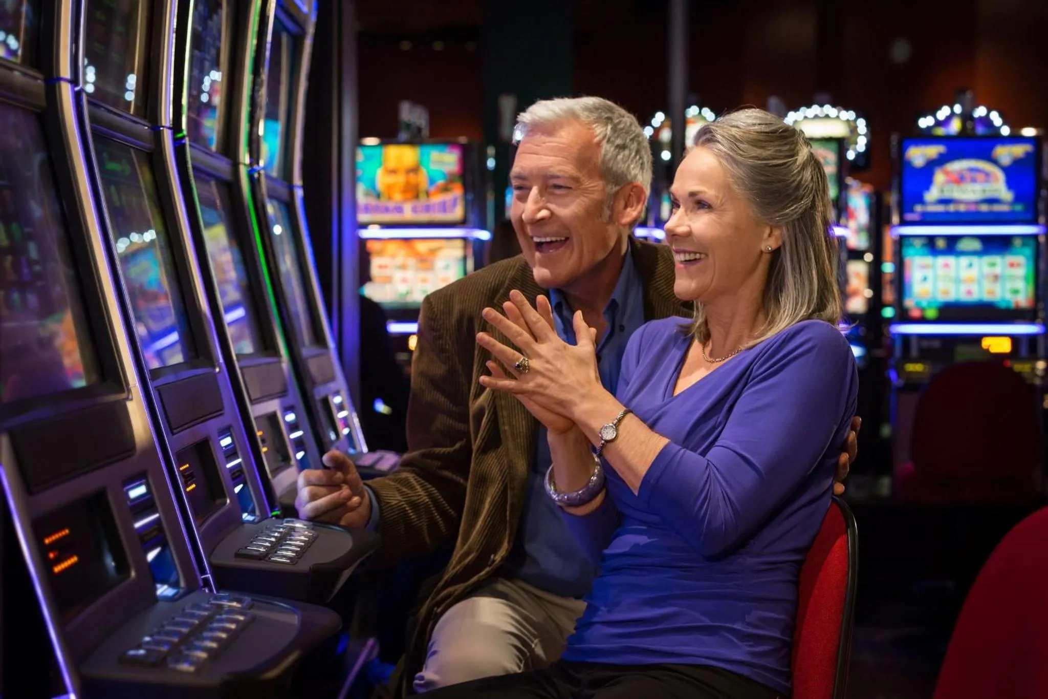 Un couple souriant joue à des machines à sous dans une salle lumineuse.