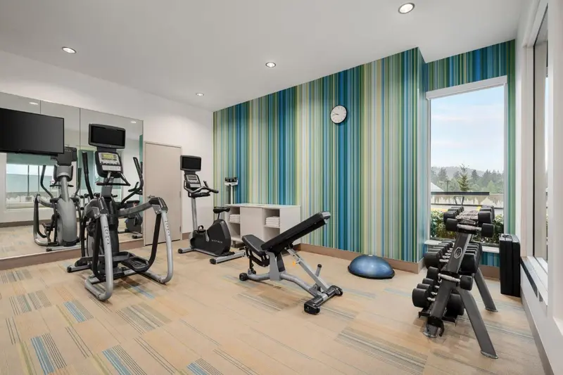 Une salle de sport lumineuse avec plusieurs appareils de musculation et un grand miroir.