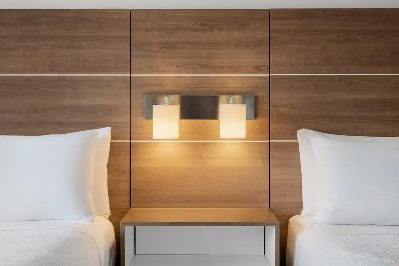 Deux oreillers blancs reposent sur un lit devant un mur en bois clair avec des lampes de chevet.