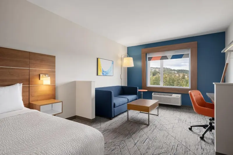 Une chambre lumineuse avec un lit, un canapé et un bureau près d'une fenêtre.