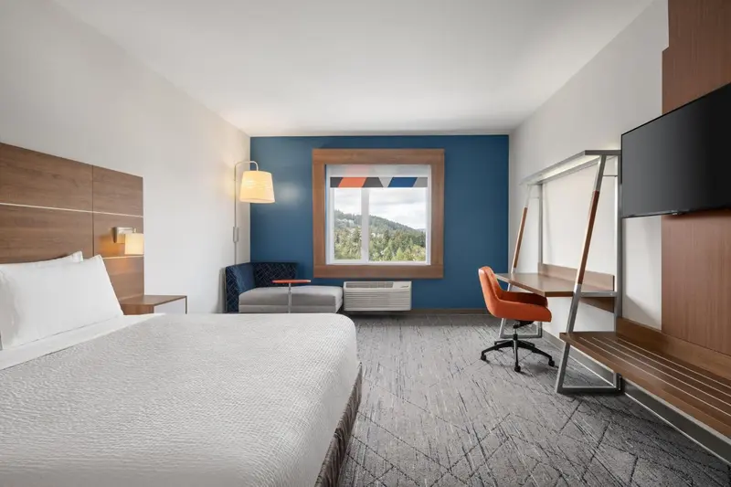Chambre lumineuse avec un lit, un bureau et une fenêtre offrant une vue sur la nature.