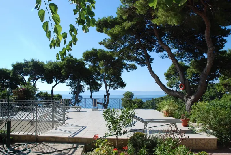 Terrasse ensoleillée avec mobilier de jardin et vue sur la mer.