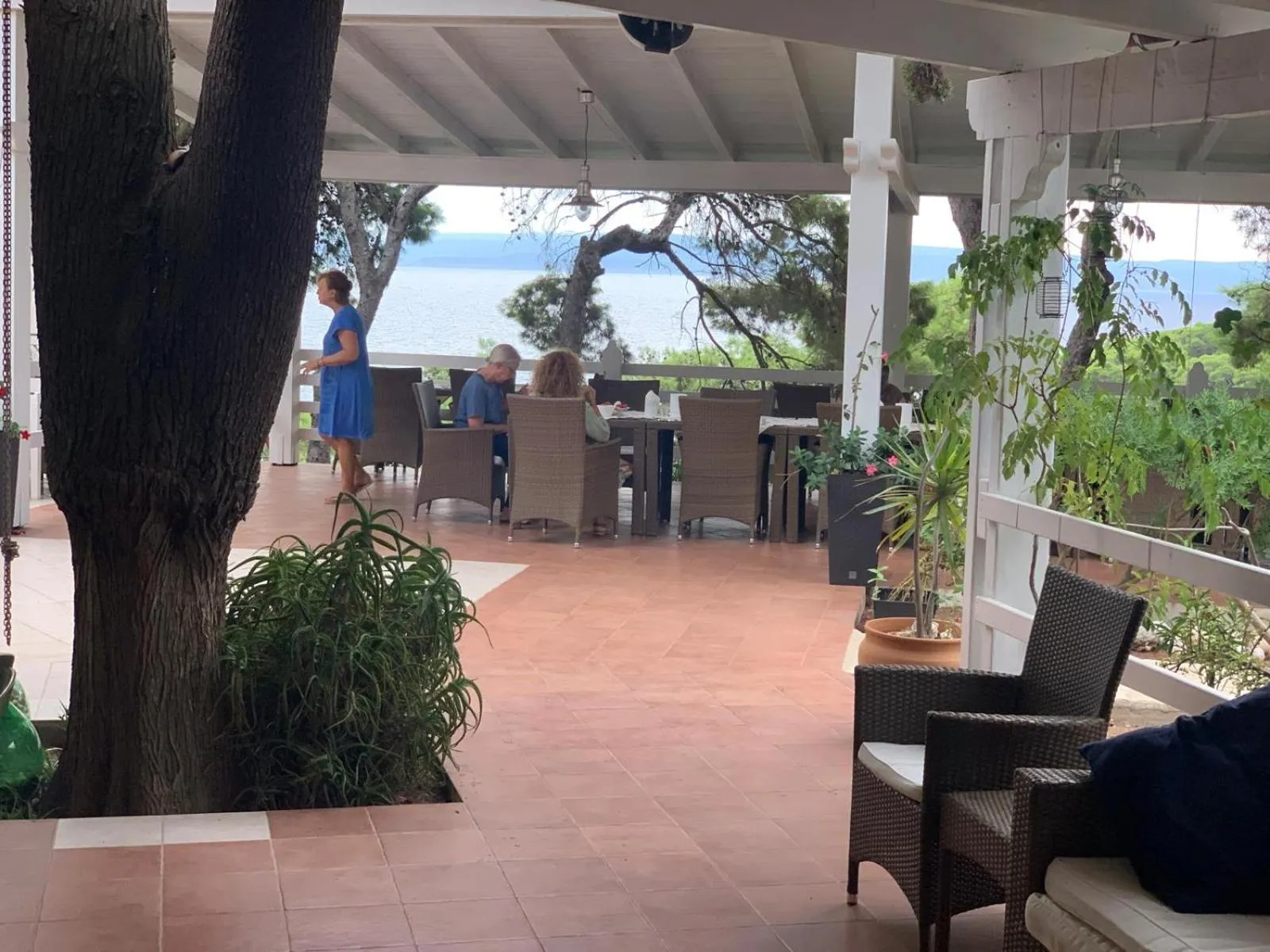 Terrasse ombragée avec tables et chaises donnant sur la mer.