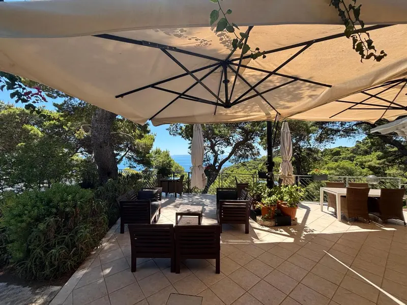 Terrasse ombragée avec mobilier de jardin et vue sur la mer.