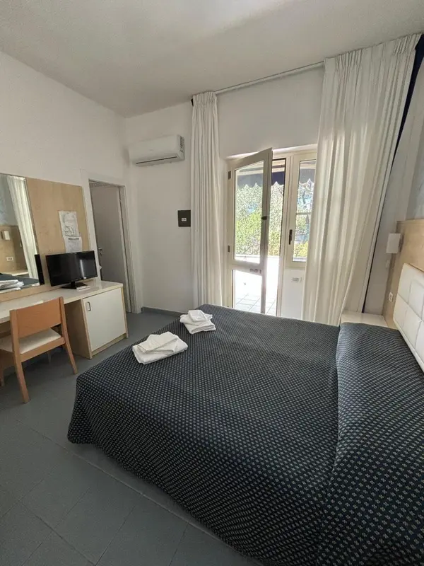 Une chambre avec un lit et un bureau près d'une porte-fenêtre.