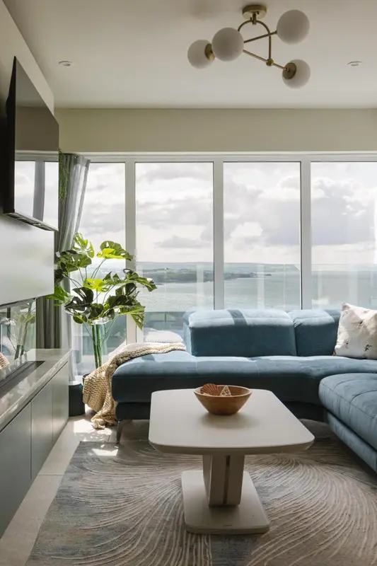 Un salon moderne avec un canapé bleu et une vue sur la mer par de grandes fenêtres.